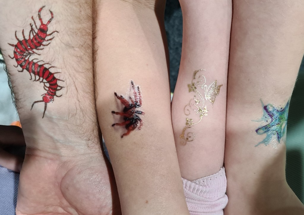 four forearms with various temporary tattoos of bugs
