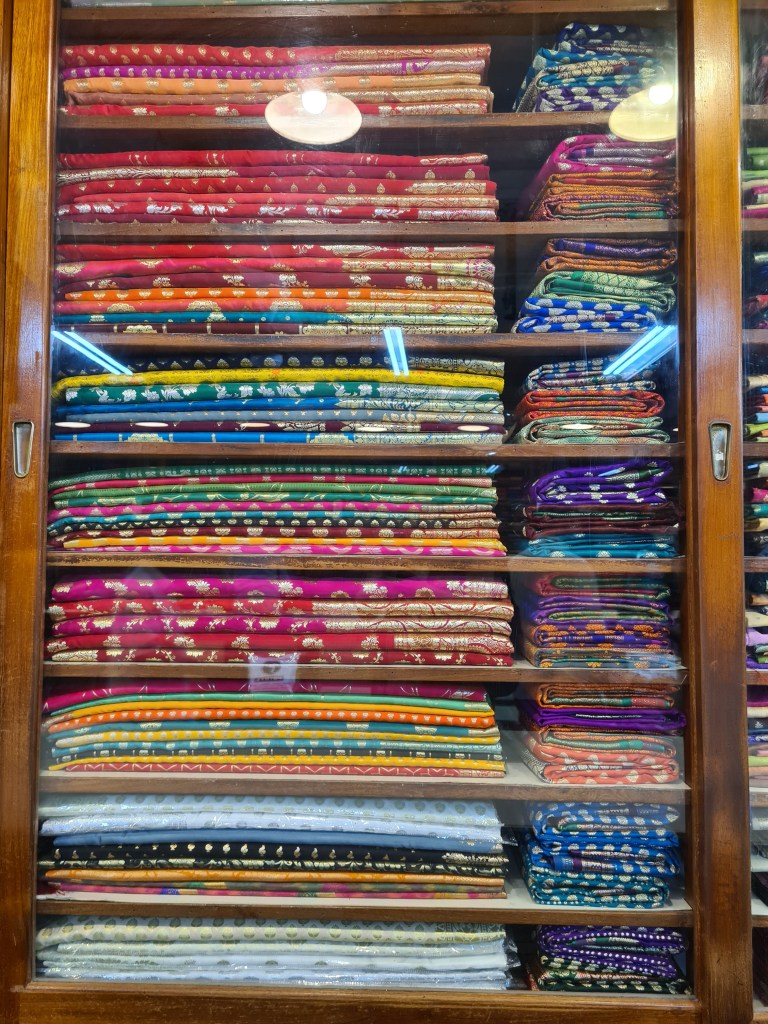 Stacks of colourful material in a glass fronted cupboard
